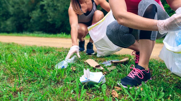 Deux femmes en habits de course ramassent des déchets laissés sur le gazon.