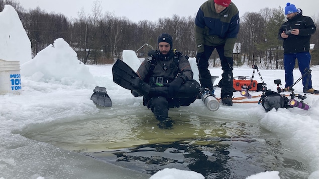 Un homme en combinaison de plongée est en train d'enfiler des palmes à ses pieds. Il est assis sur de la glace.