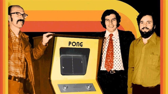 Trois hommes posent autour d'une machine sur laquelle il est écrit « Pong ». Les habits et les couleurs sont des années 70.