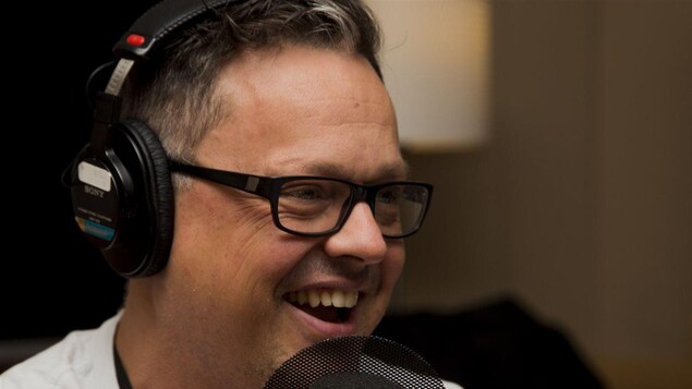 Photographié de profil, l'écrivain Éric Dupont rit alors qu'il se trouve devant un micro de studio radio. Photographié de profil, l'écrivain Éric Dupont rit alors qu'il se trouve devant un micro de studio radio.