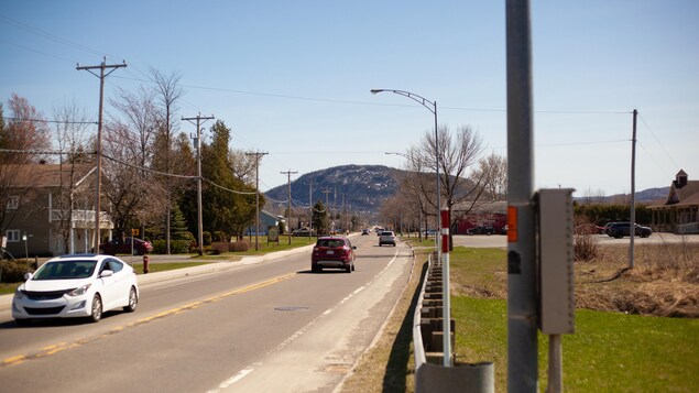 Boulevard passant dans un village. On voit une montagne en arrière-plan. 