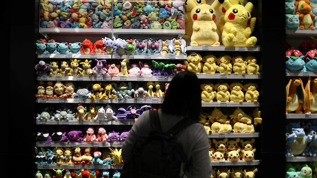 Une femme observe un présentoir rempli de peluches Pokémon. 