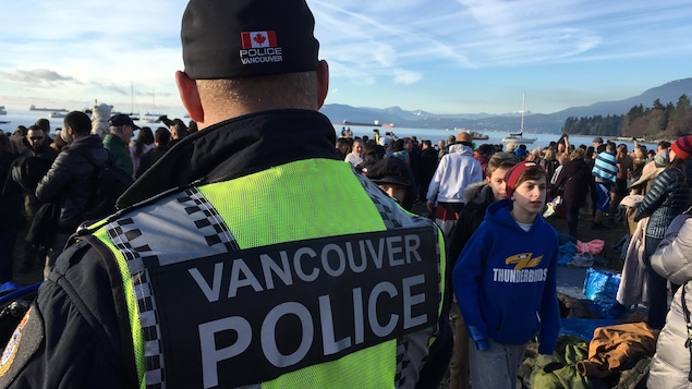 Une foule rassemblée devant de l'eau et des montagnes. La police de Vancouver surveille la foule. Une foule rassemblée devant de l'eau et des montagnes. La police de Vancouver surveille la foule.
