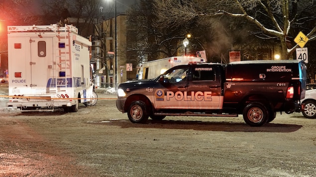Une camionnette et une grande fourgonnette du Service de police de la Ville de Montréal stationnées dans la rue l'hiver, la nuit.