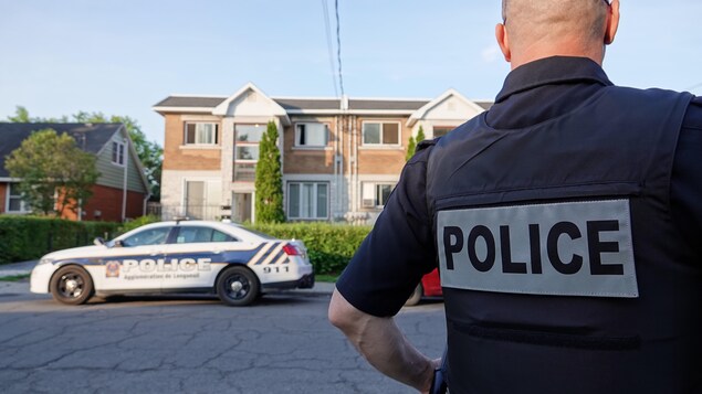 Un policier de dos se tient devant un immeuble.
