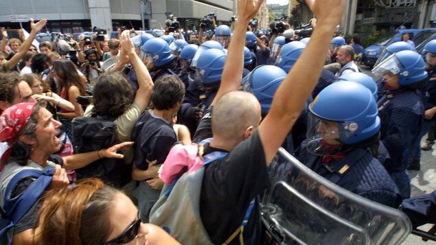 Des manifestants sont repoussés par une ligne de policiers anti-émeute dans une rue de Gênes, en Italie. Des manifestants sont repoussés par une ligne de policiers anti-émeute dans une rue de Gênes, en Italie.