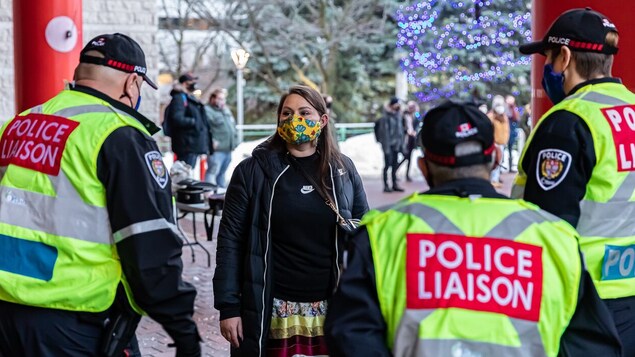 Trois policiers portant le masque discutent avec une femme portant aussi un masque.