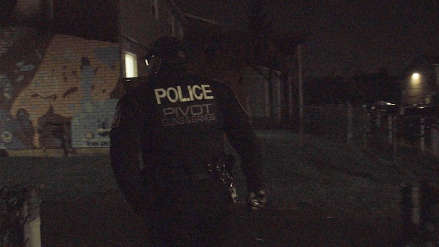 Un policier, devant un mur de graffitis.