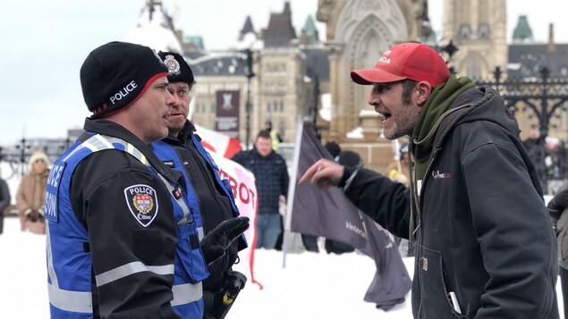 Un manifestant contfrontent deux policiers d'Ottawa sur la rue Wellington.