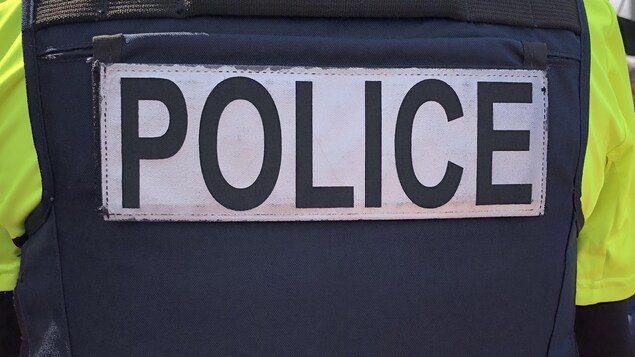 Un policier porte un uniforme où il est inscrit «POLICE».