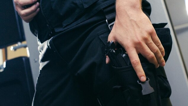 Gros plan sur le corps d'un policier qui montre sa main tenant son arme,