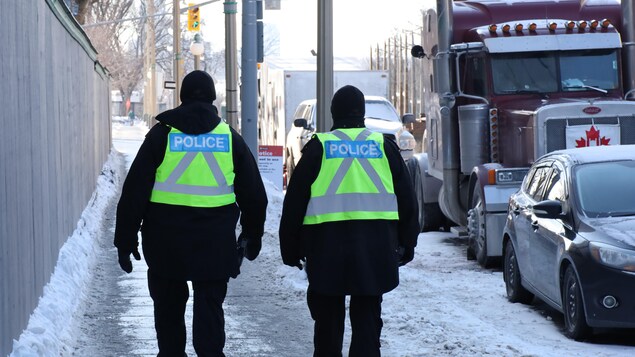 Des policiers de dos marchent sur un trottoir.