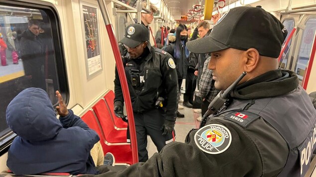 The increased police patrols on the TTC will be filled by off-duty officers who will be paid overtime, so on-duty officers can still respond to priority calls, Toronto's police chief has said. Here, two officers speak with a TTC subway rider on Friday. (Mark Bochsler/CBC)