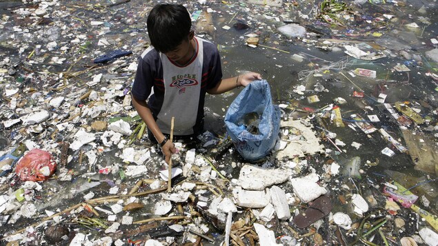 Un jeune tente de récupérer du plastique sur la côte de la ville de Manille. Il a de l'eau jusqu'à la taille et il est entouré d'une tonne de déchets qui flottent sur l'eau. Un jeune tente de récupérer du plastique sur la côte de la ville de Manille. Il a de l'eau jusqu'à la taille et il est entouré d'une tonne de déchets qui flottent sur l'eau.