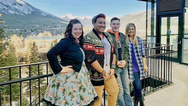 Quatre personnes se tiennent le lon d'une barrière, devant des montagnes.
