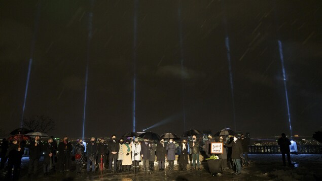 Sous un ciel sombre, Justin Trudeau, François Legault et Valérie Plante se tiennent aux côtés de proches de victimes; plusieurs ont des parapluies noirs.