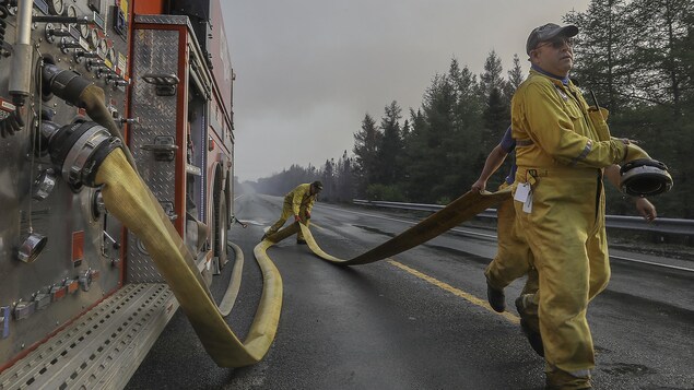 Des pompiers sur une autoroute déploient leurs boyaux d'arrosage.
