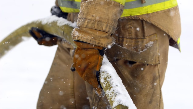 Un pompier tient un boyau d'incendie partiellement couvert de neige.