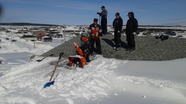 Des gens déblaient un toit avec une souffleuse à neige Des gens déblaient un toit avec une souffleuse à neige