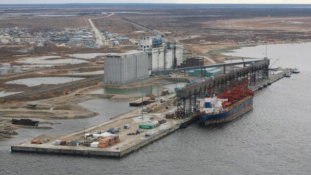 Vue aérienne d'un port avec un grand navire-cargo et des silos à grain, au beau milieu d'un paysage de toundra, en été.