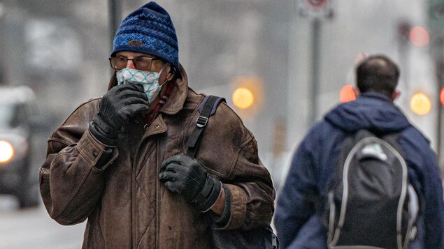 Un homme ajuste son masque, dehors, l'hiver.