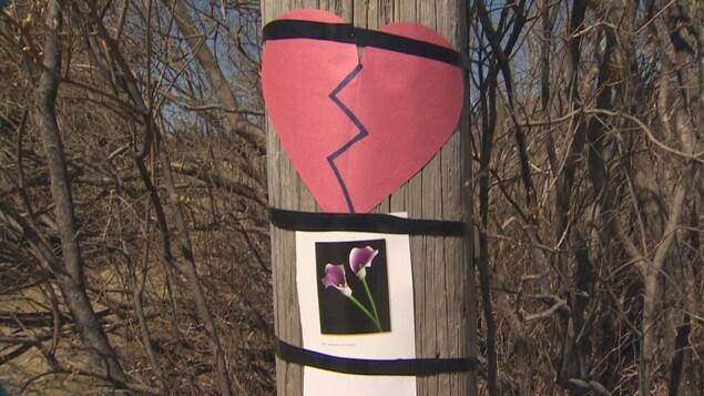 Une photo de fleurs et un coeur brisé en papier sont affiché sur un poteau électrique.