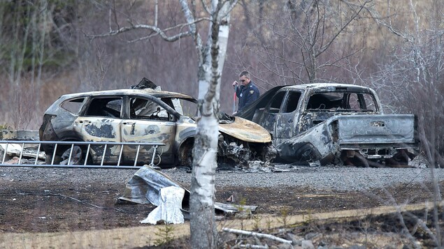 Un enquêteur entre deux véhicules complètement incendiés.