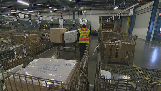 Une femme répartit des colis dans de grands bacs en métal au centre de tri du courrier d'Edmonton..