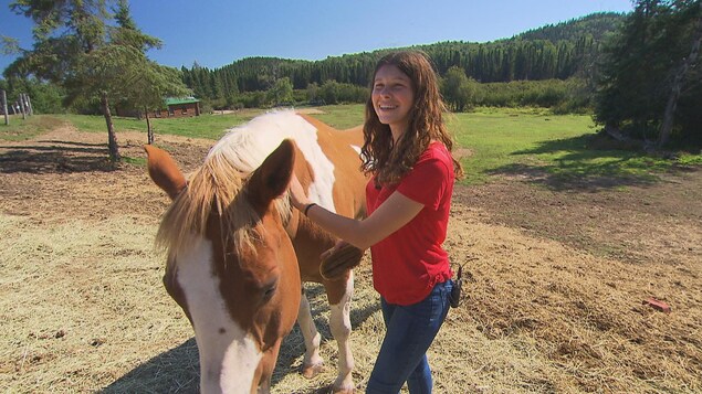 Myriam Caron, tout sourire, brosse un cheval à la robe brune et blanche. Myriam Caron, tout sourire, brosse un cheval à la robe brune et blanche.