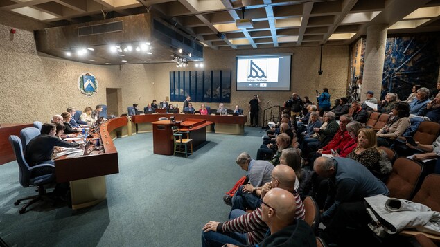 Les élus sont assis à une table devant des gradins presque remplis dans la salle du conseil.