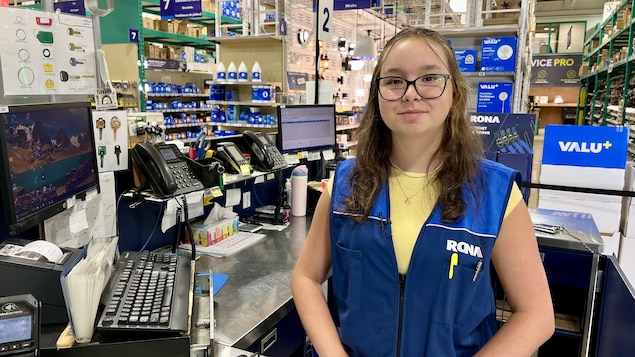L'employée est à sa caisse et sourit devant la caméra.