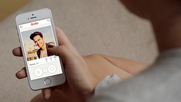 Une main tient un téléphone sur lequel est affichée l'application Tinder.