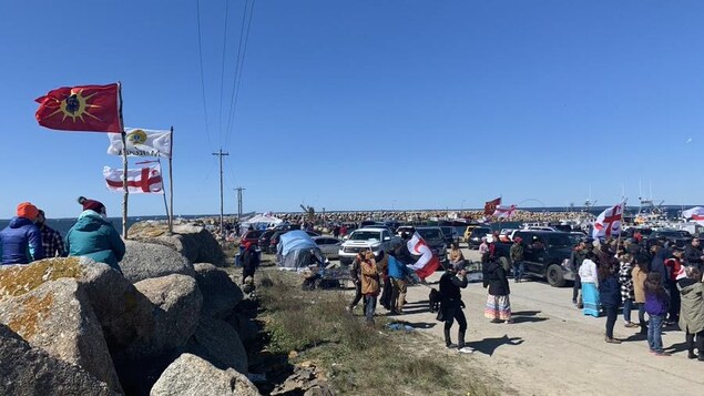 Groupes de personnes sur le quai. Plusieurs drapeaux des Nations autochtones, dont des drapeaux mi'kmaq, flottent.