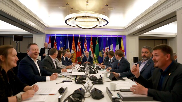 رؤساء حكومات المقاطعات والأقاليم الكندية جالسون إلى طاولة ونرى في عمق الصورة أعلام مقاطعاتهم وأقاليمهم.