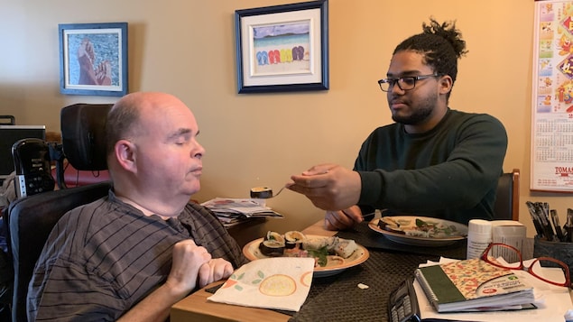 Robert Labrecque se fait nourrir par son préposé à la table de cuisine