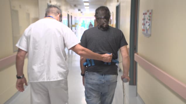 Un préposé aide un homme à marcher dans un couloir.