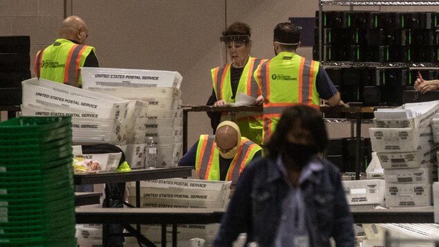 Des gens portant des masques ou des visières dépouillent des bulletins de vote dans une grande salle.