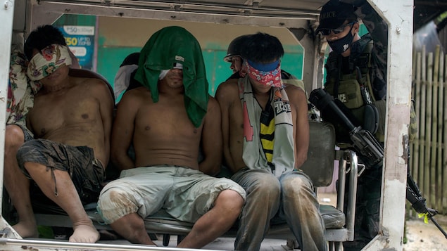 Des hommes aux yeux bandés sont entassés dans l'arrière d'un véhicule, sous la surveillance d'un soldat armé. Des hommes aux yeux bandés sont entassés dans l'arrière d'un véhicule, sous la surveillance d'un soldat armé.