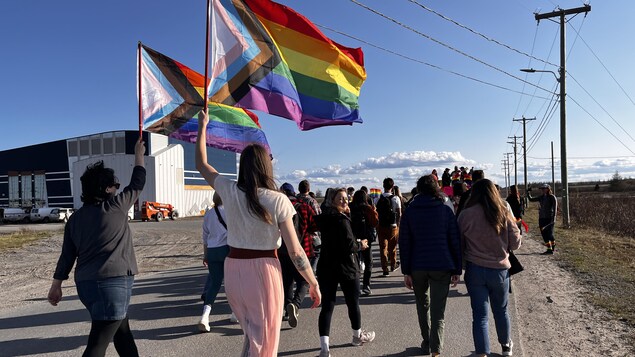 Des personnes marchent dans la rue avec un drapeau arc-en-ciel. 