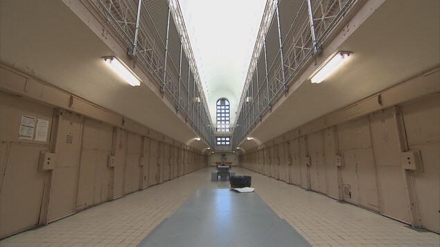 Un long corridor avec des cellules de chaque côté dont toutes les portes sont fermées.