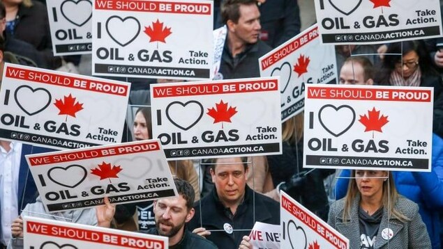 Une foule de manifestants brandit des pancartes indiquant en anglais: « we should be proud » et « I love oil and gas ».