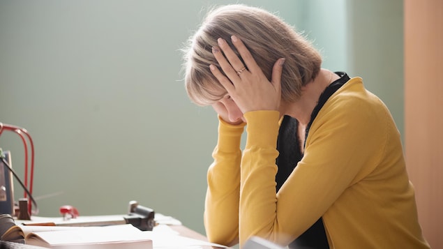 Une femme est assise à un bureau, la tête entre les mains.