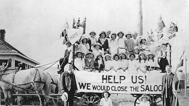 Groupe de femmes sur un chariot tiré par des chevaux et tenant une grande bannière.