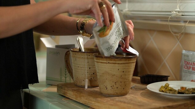 Gros plan sur les mains d'une femme qui verse le contenu d'un sachet dans une tasse posée sur un comptoir. Gros plan sur les mains d'une femme qui verse le contenu d'un sachet dans une tasse posée sur un comptoir.