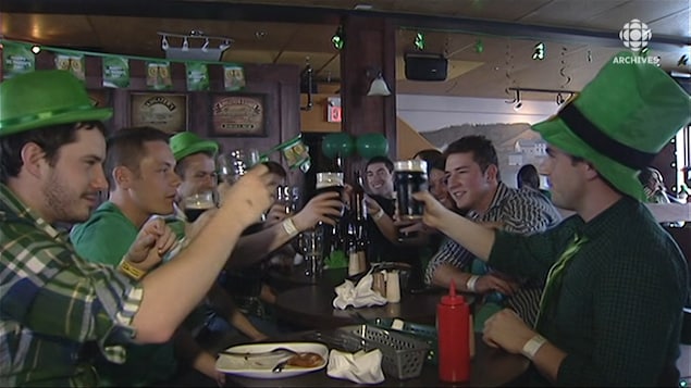 Des clients qui portent des chapeaux verts font un toast avec leurs verres de bière dans un pub irlandais.