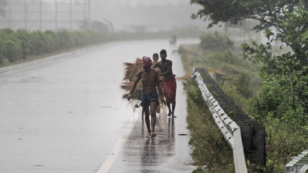 Trois hommes marchent le long d'une route sous la pluie en transportant quelques biens.