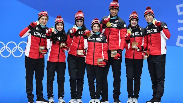 Les sept membres de l'équipe canadienne sont sur la plus haute marche du podium et montrent leurs médailles d'or.