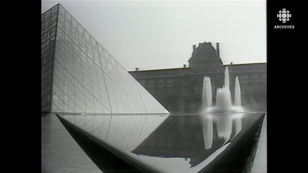 Perspective sur la pyramide de verre du Louvre encadré d'une fontaine et du bâtiment ancien original du Louvre.