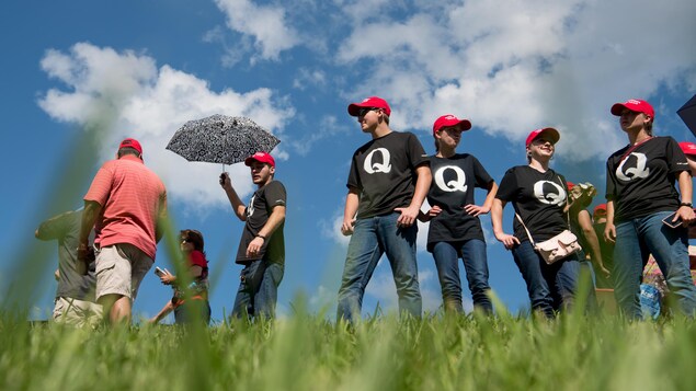 Un groupe de personnes portant des casquettes « MAKE AMERICA GREAT AGAIN » et des t-shirts noirs avec une grosse lettre Q, représentant la mouvance conspirationniste QAnon.