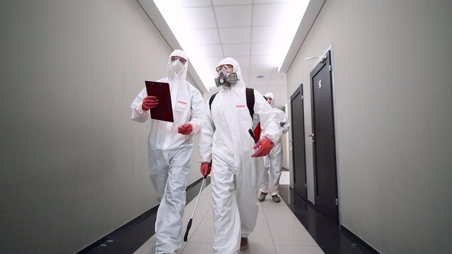 Des employés de qualinet sont vêtus d'un habit de protection blanc.